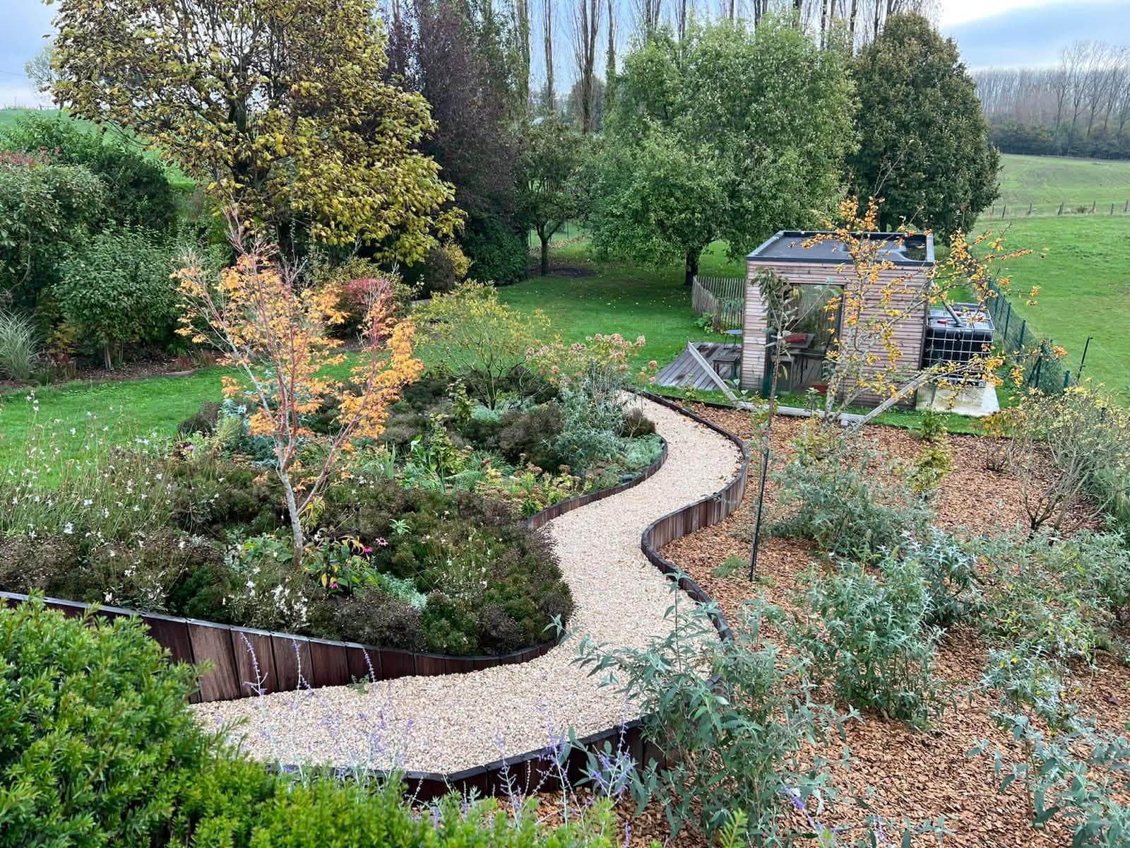 Jardin paysager avec allée sinueuse en gravier, massifs plantés et abri de jardin