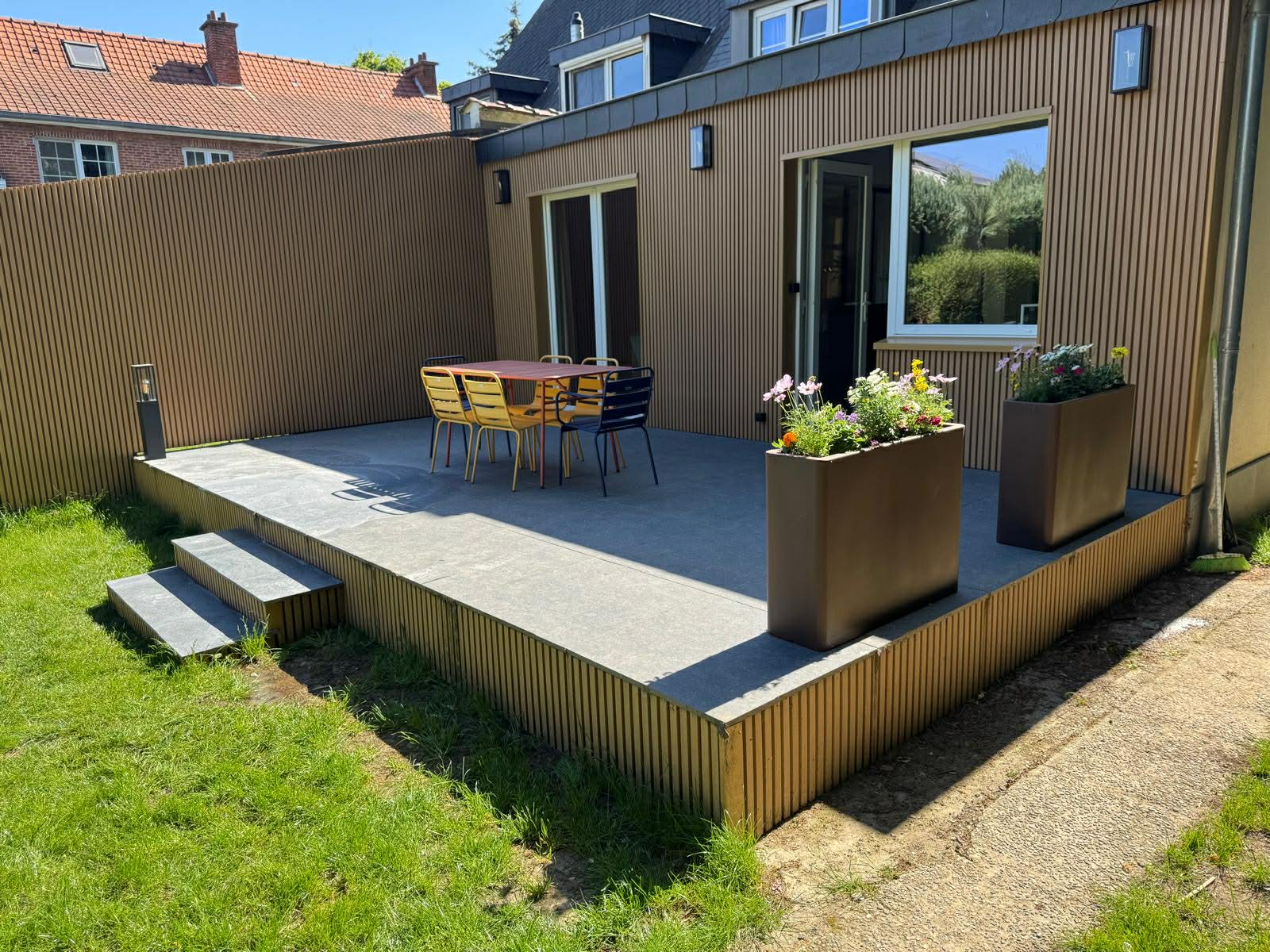 Terrasse surélevée habillée de bois, avec jardinières et marches vers la pelouse